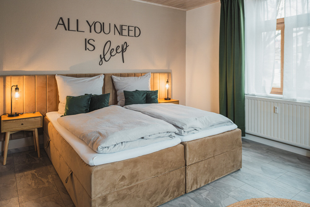 Schlafzimmer der Ferienwohnung mit Holzbett und grünen Kissen